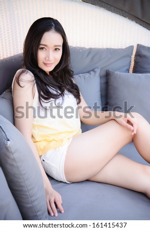Relaxing woman sitting comfortable in sofa lounge chair smiling happy looking at camera. Resting beautiful young multicultural asian caucasian girl in her 20s .
