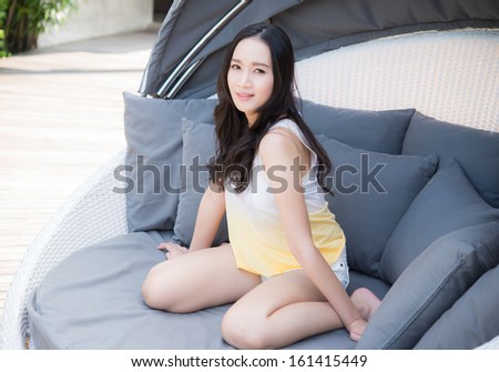 Relaxing woman sitting comfortable in sofa lounge chair smiling happy looking at camera. Resting beautiful young multicultural asian caucasian girl in her 20s .