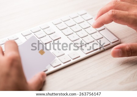 hand holding a white credit card and typing. On-line shopping on the internet