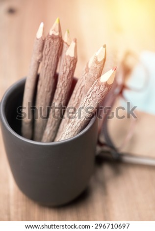 color pencil made of branches in cup with glasses and note book on wood background;vintage filter