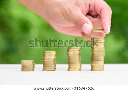 Close up of male hand stacking gold coins with green bokeh background ,Business Finance and Money concept