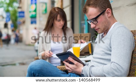 Man with cell phone and the woman with notes sitting in a cafe.  Secluded alley in a background.