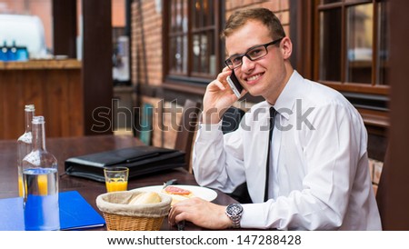 Smiling young businessman making a call with his smartphone in a restaurant.