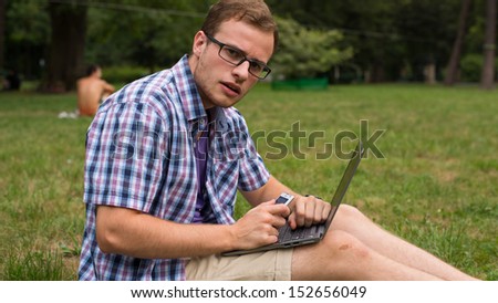 Student sitting on the grass with laptop in the park.