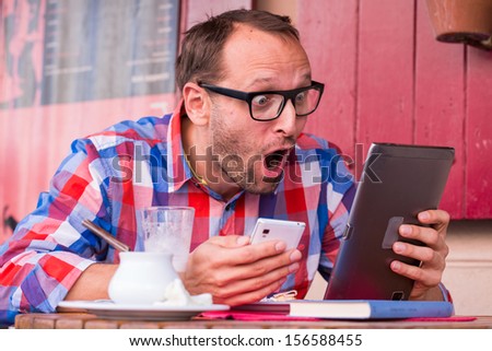 Handsome young man eating sandwich in restaurant.  He is holding a phone and tablet.