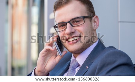 A head and shoulders shot of a 20 year old business man in a suit and shirt with tie and mobile phone.