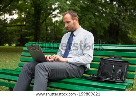 Businessman sitting on bench with laptop.