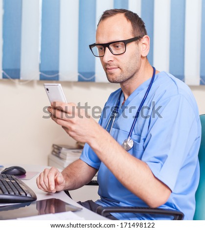 Doctor working with mobile phone in the office. He is wearing blue uniform (surgeon uniform)
