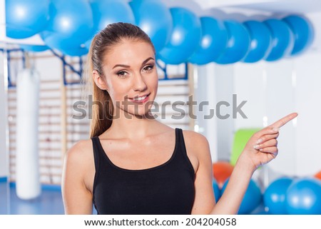 Beautiful happy young woman in gym. Gym shot. Crossfit hall. She is pointing copy space