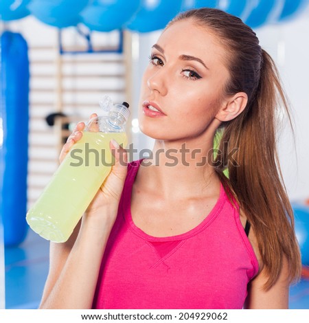 Young girl drinking isotonic drink, gym.