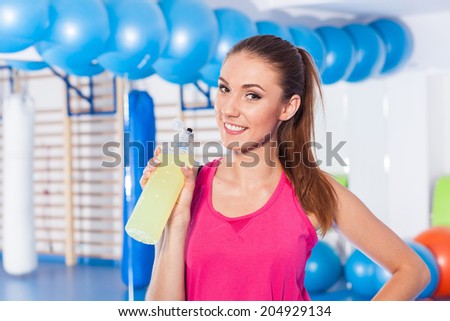 Young girl drinking isotonic drink, gym. She is happy and full of positive emotion