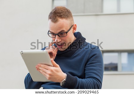 Stylish guy connected on internet with tablet in town. He is surprised. Positive emotion