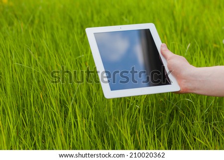 Male hand holding digital tablet on a grass field. Concep photo. Copy space. Technology in harmony with nature.