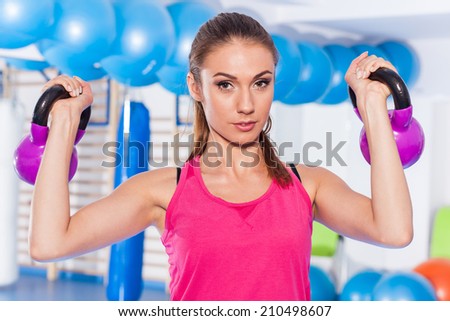 Portrait of a young pretty woman holding weights (dumbbell) and doing fitness indor. Crossfit hall. Gym shot
