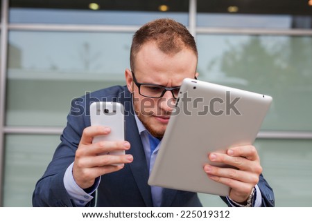 Caucasian businessman outside office using mobile phone and tablet pc on a office block background. Copy space.