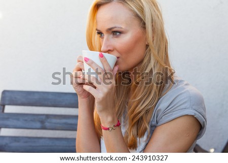 A pretty caucasian woman at home sitting on the porch and drinking coffee. She is resting. Outdoor photo.