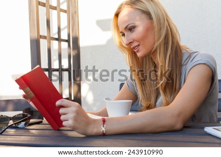 A pretty caucasian woman at home reading on the porch and drinking coffee. Outdoor photo.