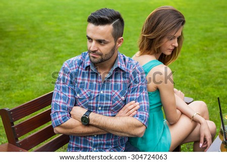 Couple sitting on the bench in the garden. They are taking offense and sitting back to back