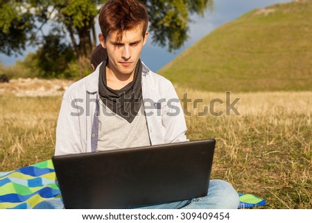 Happy young man in park writing article on his laptop