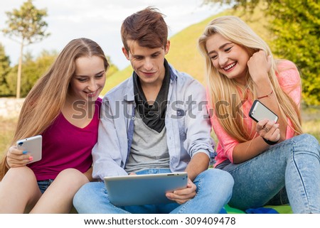 Three friends watching funny movies on tablet pc in park