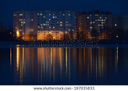 Late evening landscape with the illuminated apartment houses and gleams on water surface. City night photography: illuminated apartment buildings and reflections on water reservoir