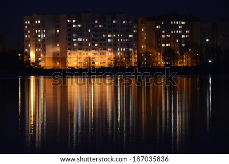 Beautifully-looking night landscape with the illuminated apartment houses and gleams on water surface. City night photography: illuminated apartment buildings and reflections on water reservoir