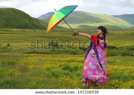 Young lady standing on grassland full of yellow flowers with colorful rainbow umbrella
