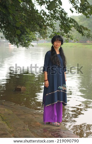 Young lady in Chinese traditional clothes, standing by a river in an ancient town