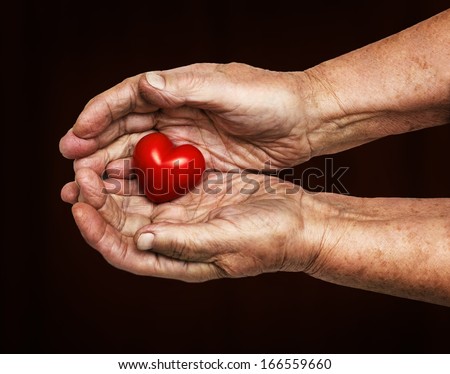 elderly woman keeping red heart in her palms isolated on dark background, symbol of care and love