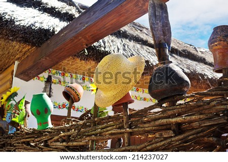 Related structure twigs and sticks in a wooden rural fence with creative household items - old clay pots for cooking and straw hat near house