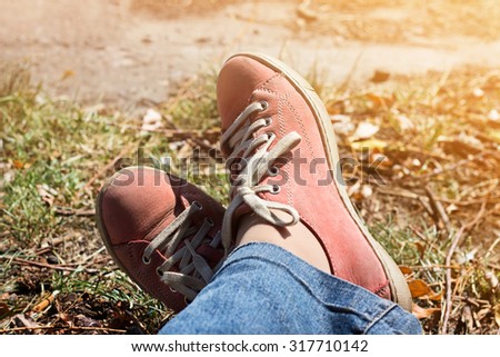 Legs crossed in red sneakers and jeans outdoors. Relax in autumn park.