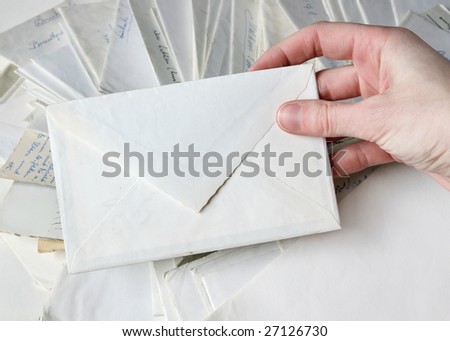 Hand holding a blank white envelope. Many other letters visible in the background.
