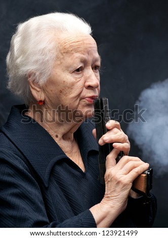 Old woman with pistol on a gray background