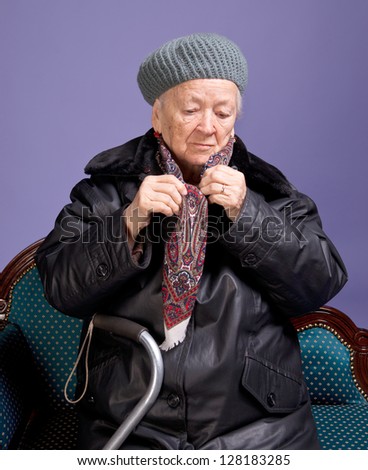 Old woman adjusting her scarf on a lilac background