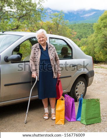 Old woman standing with shopping bags near the car