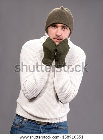 Handsome man in winter mittens and hat on a gray background