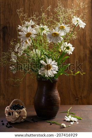 Bouquet of daisies in vase and blueberries in basket
