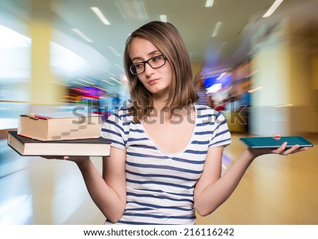 Pretty young girl holding a book in one hand and a tablet-pc in the other