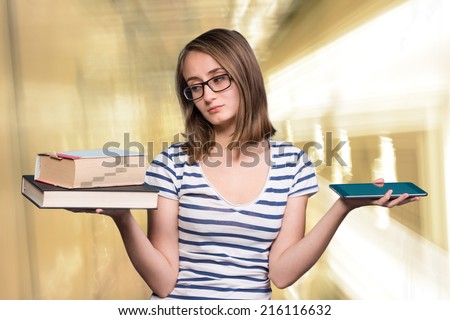 Pretty young girl holding a book in one hand and a tablet-pc in the other