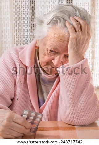Old sad woman holding pills at home