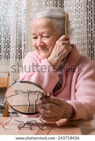 Portrait of old smiling woman combing her hair at home