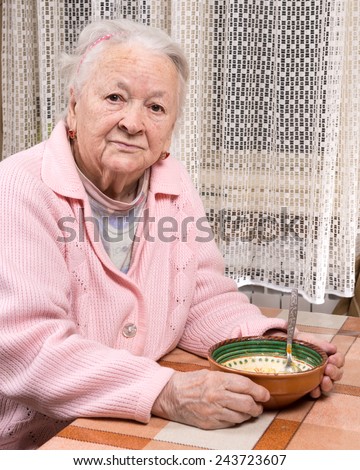Old sad woman eating at home