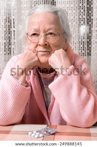 Old sad woman with pills at home. Worried about having to take too many pills