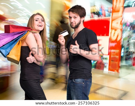Happy couple with shopping bags in the mall. Man holding credit card