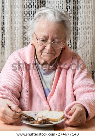 Old sad woman in glasses eating at home