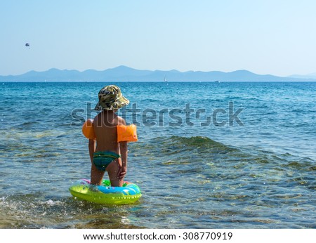 Little boy in inflatable arm ring and swimming circle standing in the sea