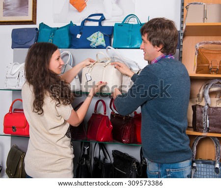 Shop assistant showing white leather bag to woman at the mall