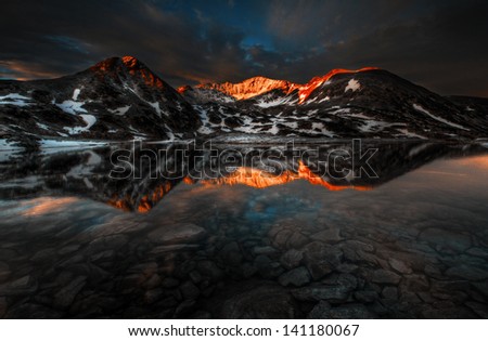 Massive Retezat mountains sunset reflection in crystal clear lake with rocks