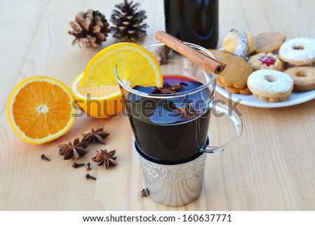 Mulled wine in glass mug, spices, cookies and orange on wooden table. Shallow DOF.