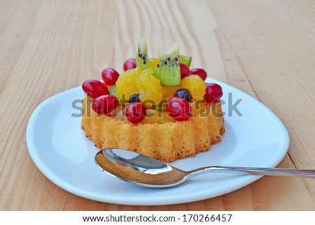 Dessert, sponge cake flan filled with forest fruits, kiwi and custard on plate, over wooden table.